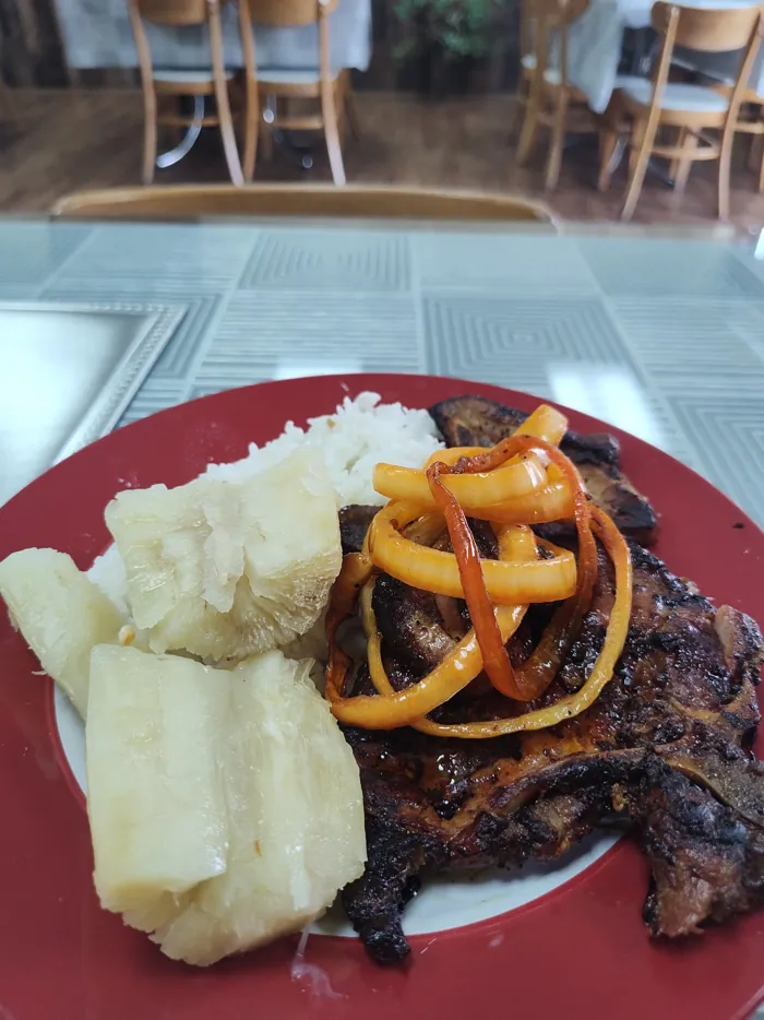 Pork chop topped with onions and peppers, served with yuca and rice