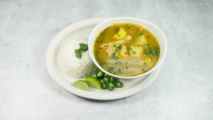 Bowl of hen soup with rice and lime on the side